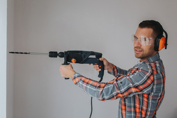 Builder worker with equipment making hole in wall at construction site
