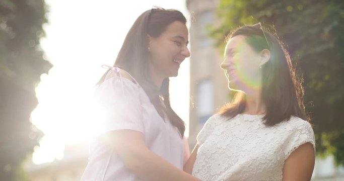 Two pretty caucasian sisters smiling and hugging in the city park. Outdoors.