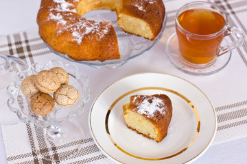 Cupcake with powdered sugar in a vase. A slice of cake on a white dish. Almond cookies in a glass vase. Herbal tea.