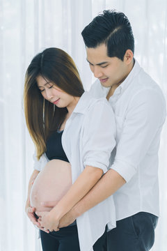 Beautiful pregnant woman and her handsome husband hugging and smiling