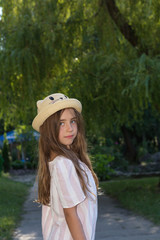 Cute little girl in a funny hat posing in the city park on a sunny summer day