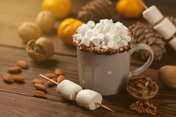 mug with hot chocolate served with chunks of mandarins, nuts, marshmallow, cones, cinnamon on old wooden table