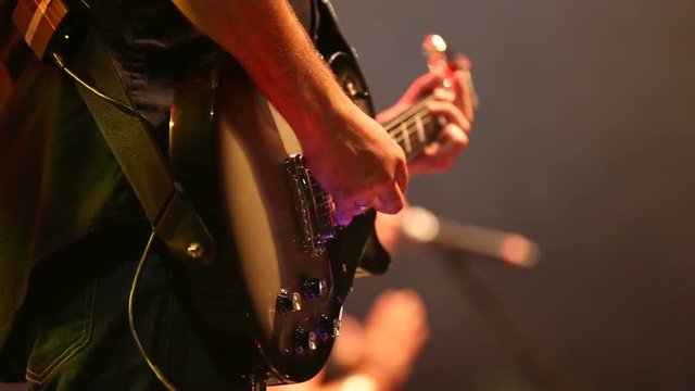 Guitar Player Playing with Singer in Background. a closeup profile shot of a guitar on stage with a singer in background blurred
