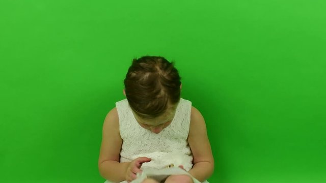 Cute small girl uses mobile phone on chroma key background. Little girl dressed in a romantic dress. White wedding dress. Chroma key background.