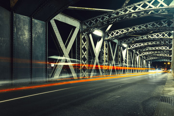 Asphalt road under the steel construction of a bridge in the city. Night urban scene with car light...