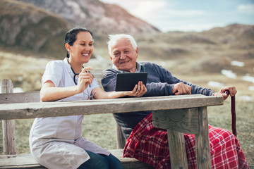 Smiling caregiver nurse and  disabled senior patient using digital tablet and credit card outdoor