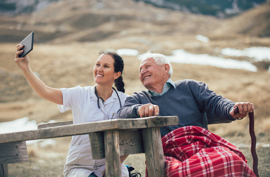 Smiling caregiver nurse and  disabled senior patient using digital tablet outdoor