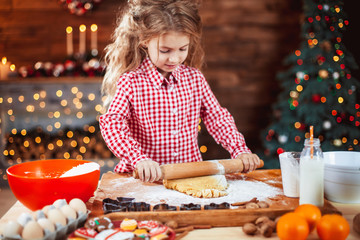 Happy little child, cute kid girl at the table in domestic kitchen making gingerbread xmas cookies decorated for Christmas holiday. Girl helping and having fun