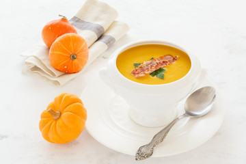 cream soup from vegetables pumpkin, leeks, carrots with Parmesan,  bacon, parsley in a white soup plate. still life covered table view from above.
