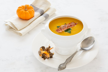 cream soup from vegetables of a pumpkin, a leek, carrots with a Parmesan, mushroom and bacon, a parsley in a white soup plate. still life covered table view from above.