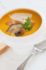 cream soup of pumpkin vegetables, leeks, carrots with Parmesan, white mushroom and bacon in a white soup plate. still life covered table view from above.