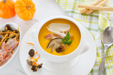 cream soup of pumpkin vegetables, leeks, carrots with Parmesan, white mushroom and bacon in a white soup plate. still life covered table view from above.