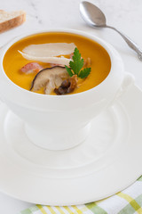 cream soup of pumpkin vegetables, leeks, carrots with Parmesan, white mushroom and bacon in a white soup plate. still life covered table view from above.