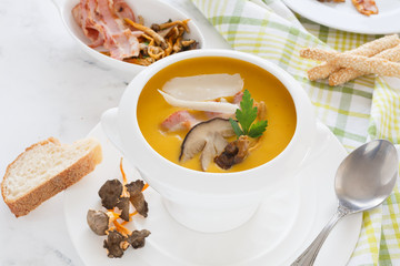 cream soup of pumpkin vegetables, leeks, carrots with Parmesan, white mushroom and bacon in a white soup plate. still life covered table view from above.