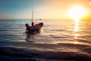 Beautiful seascape view the fishing boat floating on the sea with sunset light in the background. (Selective focus)
