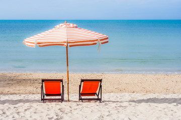 Vacation Concept : Two red wooden chairs and beach umbrella setting on white sand with seascape and blue sky in the background.