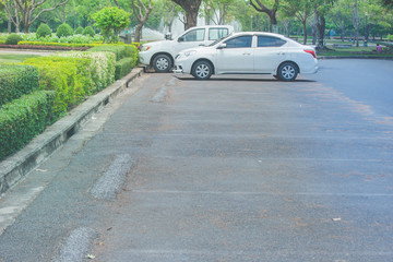 Group of cars parked on concrete floor at car parking lot surrounded with green natural at public park.