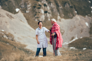 Nurse helping elderly senior man to walk on frash air outdoor.