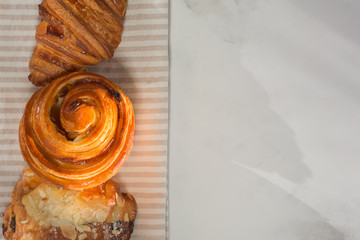a still-life of fresh French baking croissant, rolls with almond puree and snails with custard and raisins lying on a napkin top view.