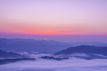 The top view of the silhouettes and peaks of the mountains at dawn, sunset, the rising sun from behind the mountains, a beautiful dawning colorful sky. Lovely mountain spacious landscape.

