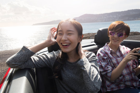 Young women sitting in convertible car at beach