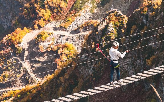 Fototapeta Unidentified girl in helmet walking along rope bridge hanging over abyss in mountains of Krasnaya Polyana, Russia