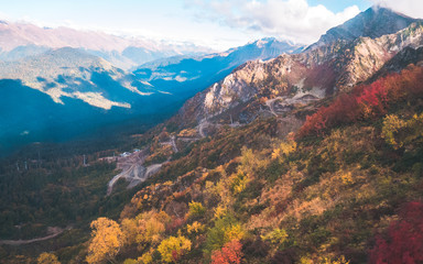 Colorful autumn forests covering slopes of magnificent Caucasus mountains on bright sunny day. Krasnaya Polyana, Russia