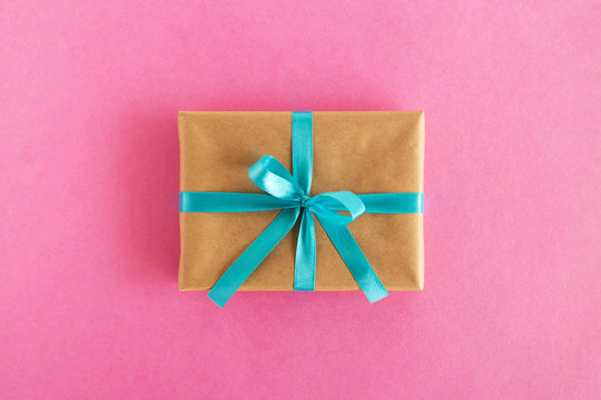 Gift box wrapped of craft paper and blue ribbon on the pink background, top view.