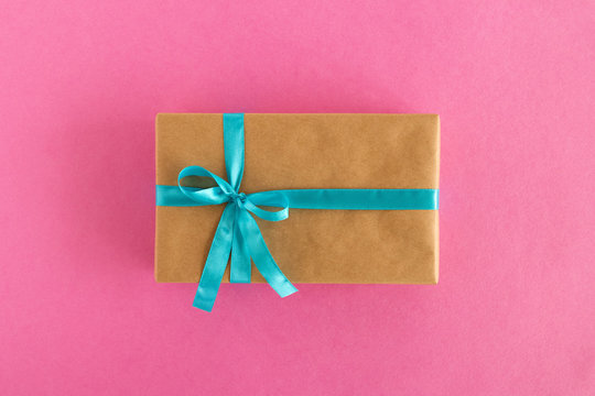 Gift box wrapped of craft paper and blue ribbon on the pink background, top view.