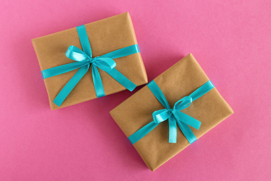 Two gift boxes wrapped of craft paper and blue ribbon on the pink background, top view.