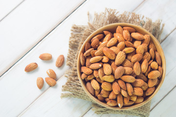 Almonds in brown bowl on wooden background