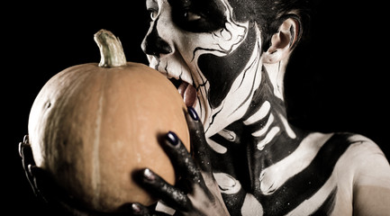 Attractive girl with skeleton makeup holds a pumpkin