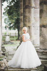 Beautiful elegant bride with perfect wedding dress and bouquet posing near old castle