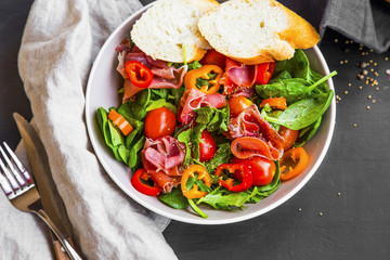 Fresh prosciutto ham salad with tomatoes , lettuce, spinach and pepper in a bowl