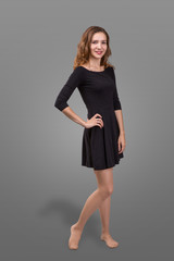 Fototapeta premium Beautiful woman standing in a black dress over gray background