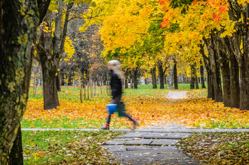 Motion blur silhouette of a fast-moving girl in an autumn park. Long exposure abstract background. Rush concept