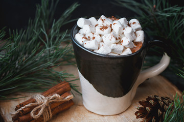 New Year and Christmas concept. Hot chocolate with marshmallow in a clay black and white mug on an old wooden board decorated with spruce branches and cinnamon sticks.