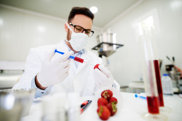 Protected lab worker doing a test with red liquid and strawberry with a syringe.