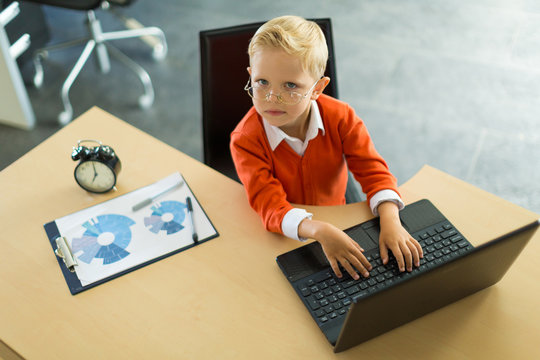 Cute boy sit at the desk in the office and uses computer