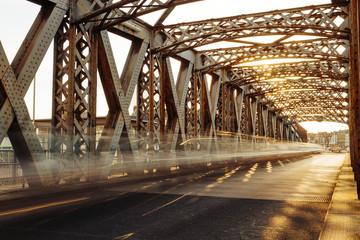 Asphalt road under the steel construction of a city bridge on a sunny day. Urban scene in the bridge tunnel. Long exposure. Toned