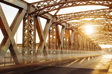 Asphalt road under the steel construction of a city bridge on a sunny day. Urban scene in the bridge tunnel. Long exposure. Toned