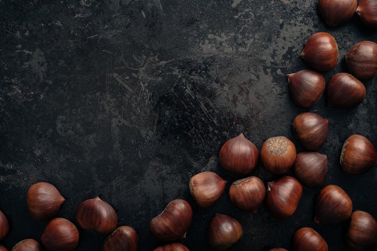Chestnuts on dark black rustic background. Pile of fresh chestnuts ready to roast shot over black antique background. Top view, copy space.