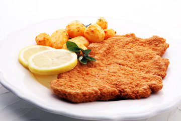 Golden schnitzel, boiled potatoes and lemon on a plate.