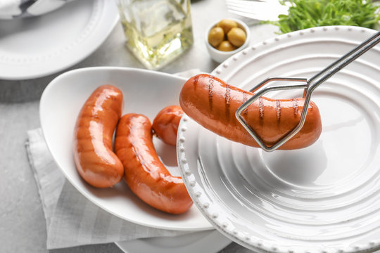 Tongs holding grilled sausage over plate