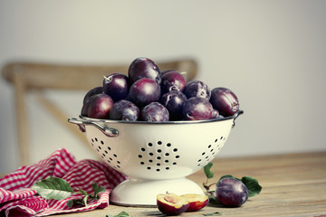Fresh plums in colander on table