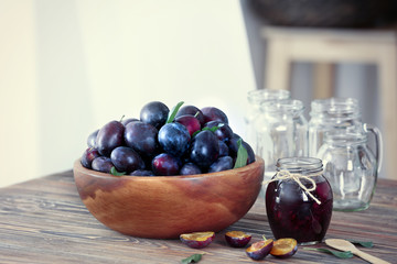 Bowl with plums and jar of jam on table