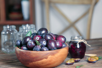 Bowl with plums and jar of jam on table