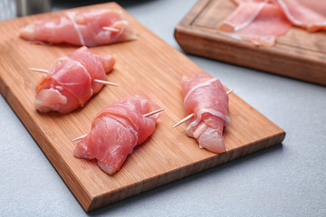 Raw bacon wrapped chicken on wooden board