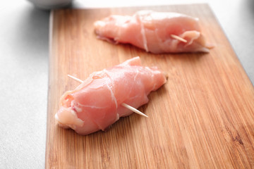 Raw bacon wrapped chicken on wooden board