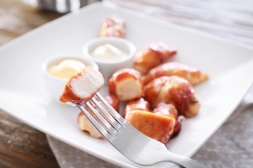 Fork with bacon wrapped chicken on blurred background, closeup